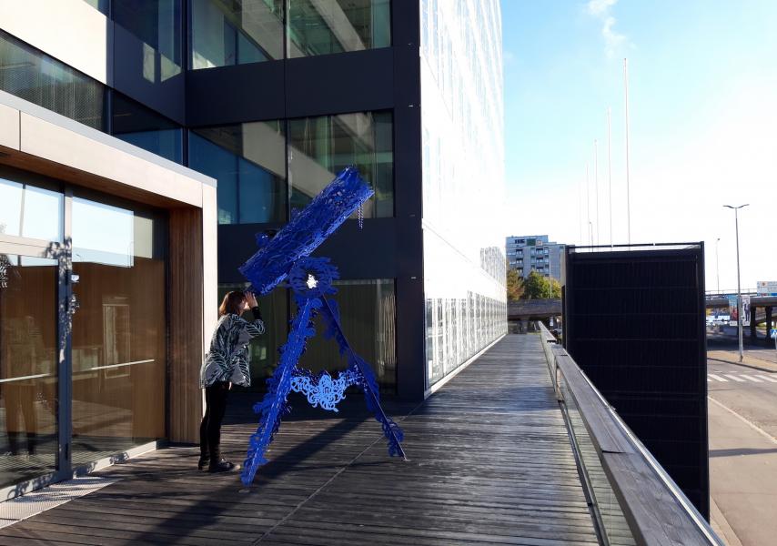 Henkilö seisoo kaukoputkea muistuttavan taideteoksen vieressä rakennuksen edessä.