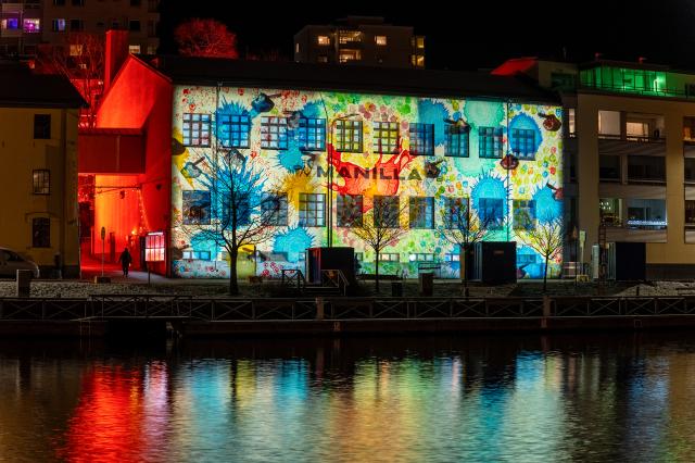 Immanuel Pax: Flower Power. Valoteos valotapahtumassa Valon polku, Turku 2024. Valokuvaaja: Rami Saarikorpi. Valaistu rakennus joen varrella